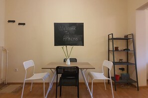 A room with a table, two chairs, a blackboard with 'Welcome to Athens' written on it, a vase with plants, and a metal shelf with various items. - Vacation Home For 4 - ENTIRE FLAT (Athina)