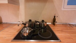 Une cuisine équipée d’une plaque de cuisson à induction noire, de trois casseroles en acier inoxydable, d’une bouilloire et d’une bouteille d’huile d’olive posée sur le plan de travail.