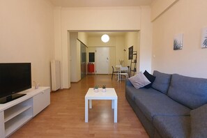 Un salon doté d’un téléviseur à écran plat, d’un canapé gris, d’une table basse blanche et d’un coin repas à l’arrière-plan.