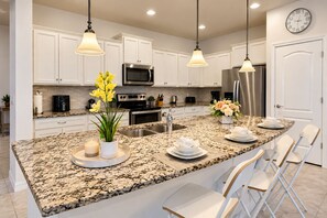 A modern kitchen with white cabinetry, granite countertops, stainless steel appliances, and pendant lighting.