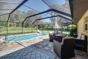 Ein überdachter Außenbereich mit Pool, Korbmöbeln und Blick auf den umliegenden Garten.