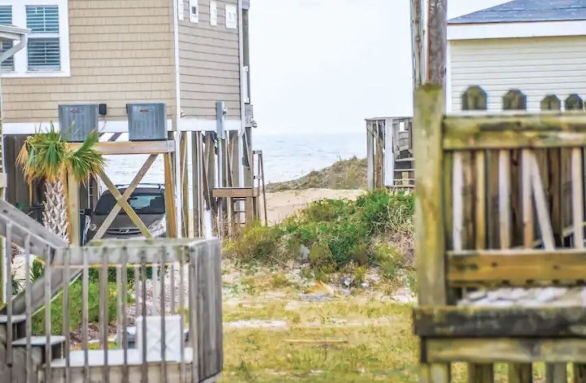 A beachfront property with a wooden deck, a parked car, and a view of the ocean.