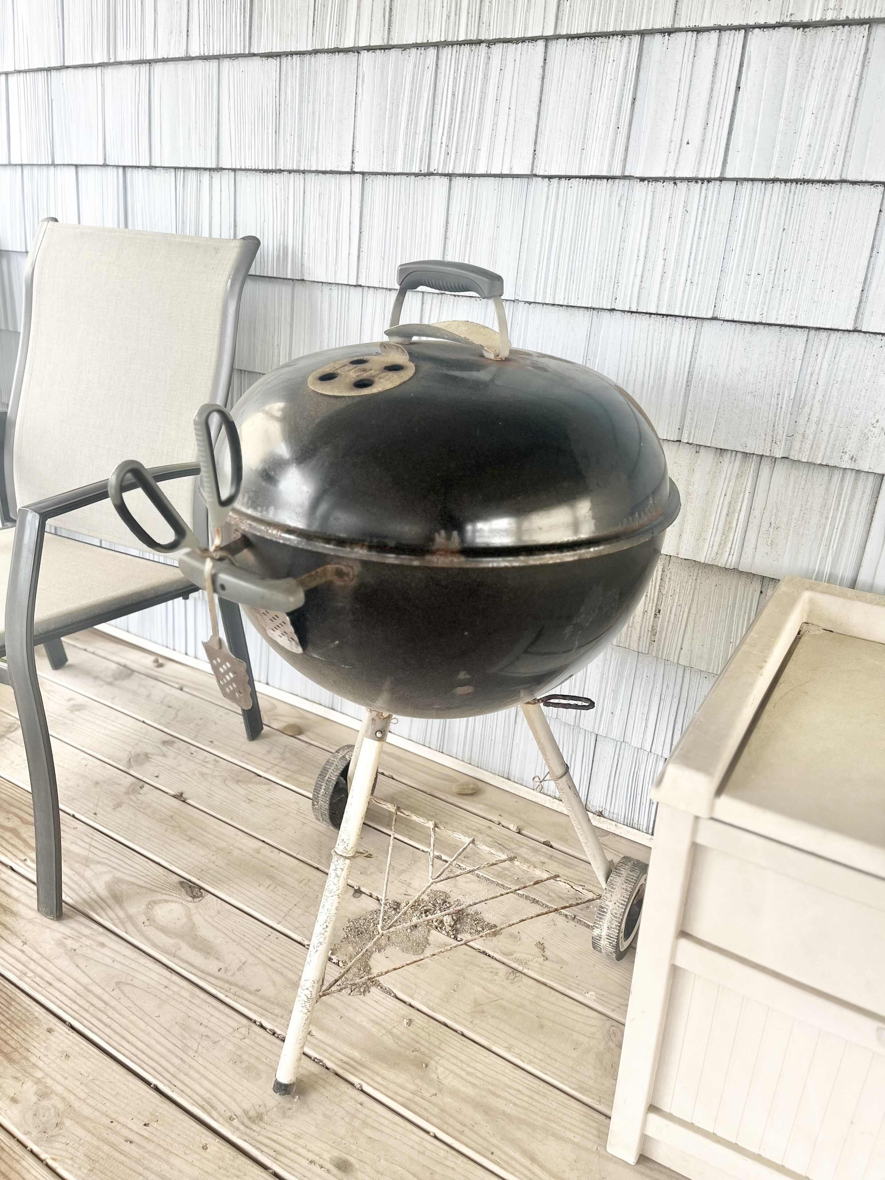 A portable grill with a lid, placed on a wooden deck.