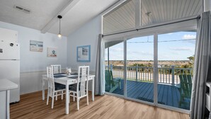 A spacious room with a large sliding glass door leading to an outdoor deck, a white dining table with chairs, and a ceiling fan. - Pets OK Beach Home+Short Walk Beach Access+Views! Recent Updates & Upgrades (Surf City)