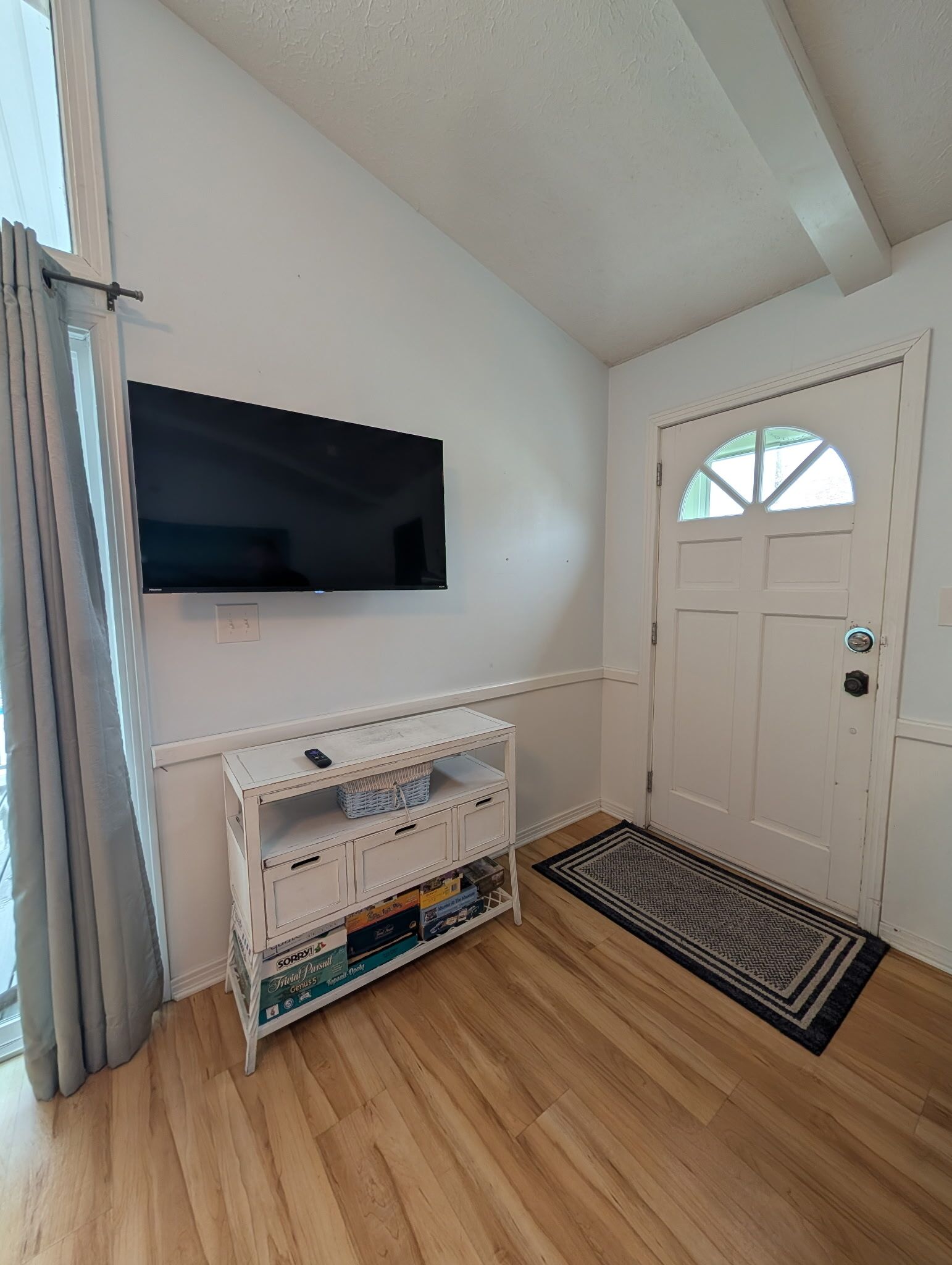A room with a white door, a mounted flat-screen TV, a white console table with storage boxes, and a black and white rug.