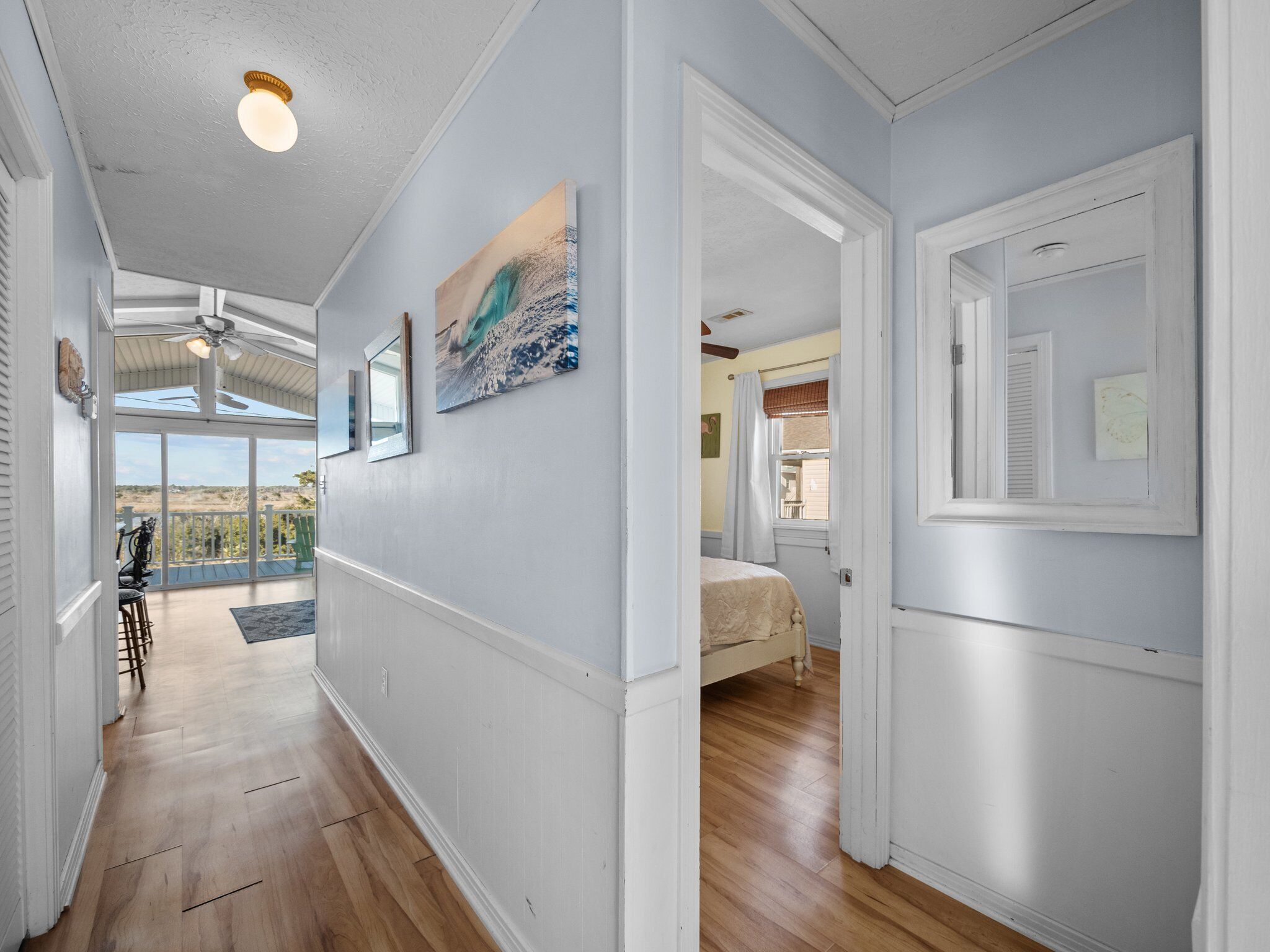 A hallway with a ceiling fan, a painting, and a view to a balcony with outdoor furniture.
