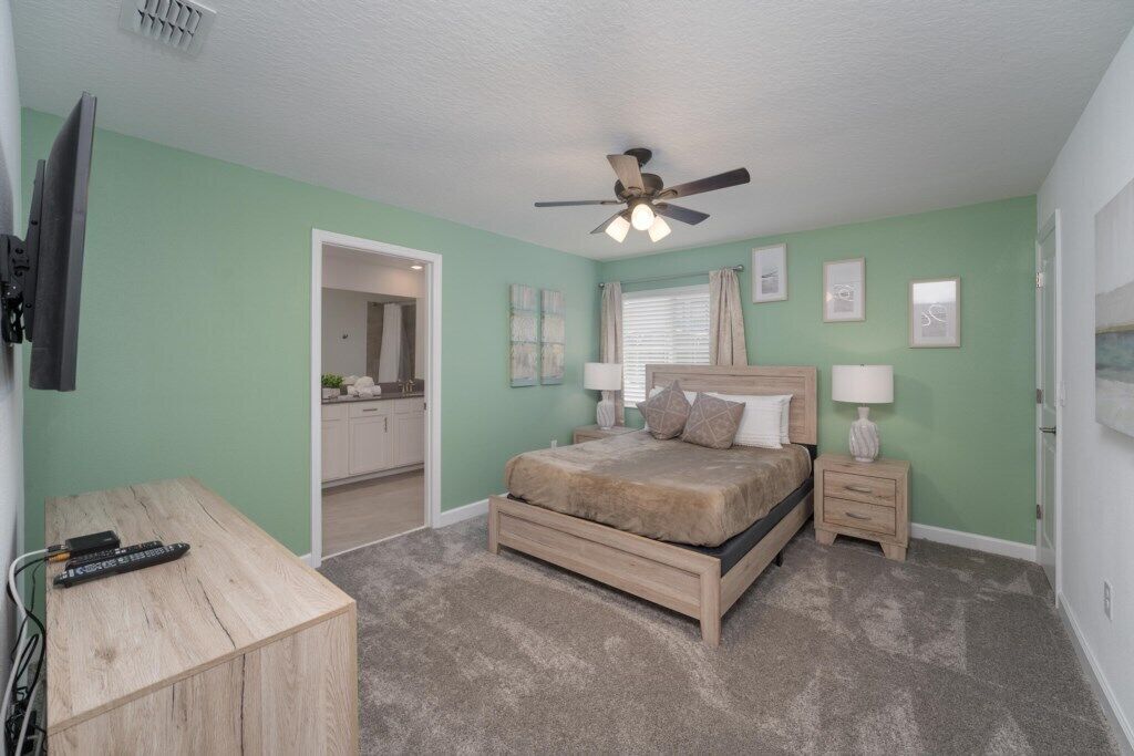 A bedroom with a bed, bedside tables, a ceiling fan, and a TV mounted on the wall.