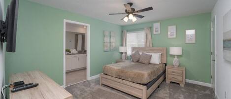 A bedroom with a bed, bedside tables, a ceiling fan, and a TV mounted on the wall.