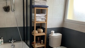 A bathroom with a bathtub, a toilet, a shower, and a wooden shelf with towels. - T4 family home 3 km from the beach (Anglet)