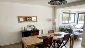 A dining area with a wooden table and chairs, a mirror above the table, and a sofa in the background. - T4 family home 3 km from the beach (Anglet)
