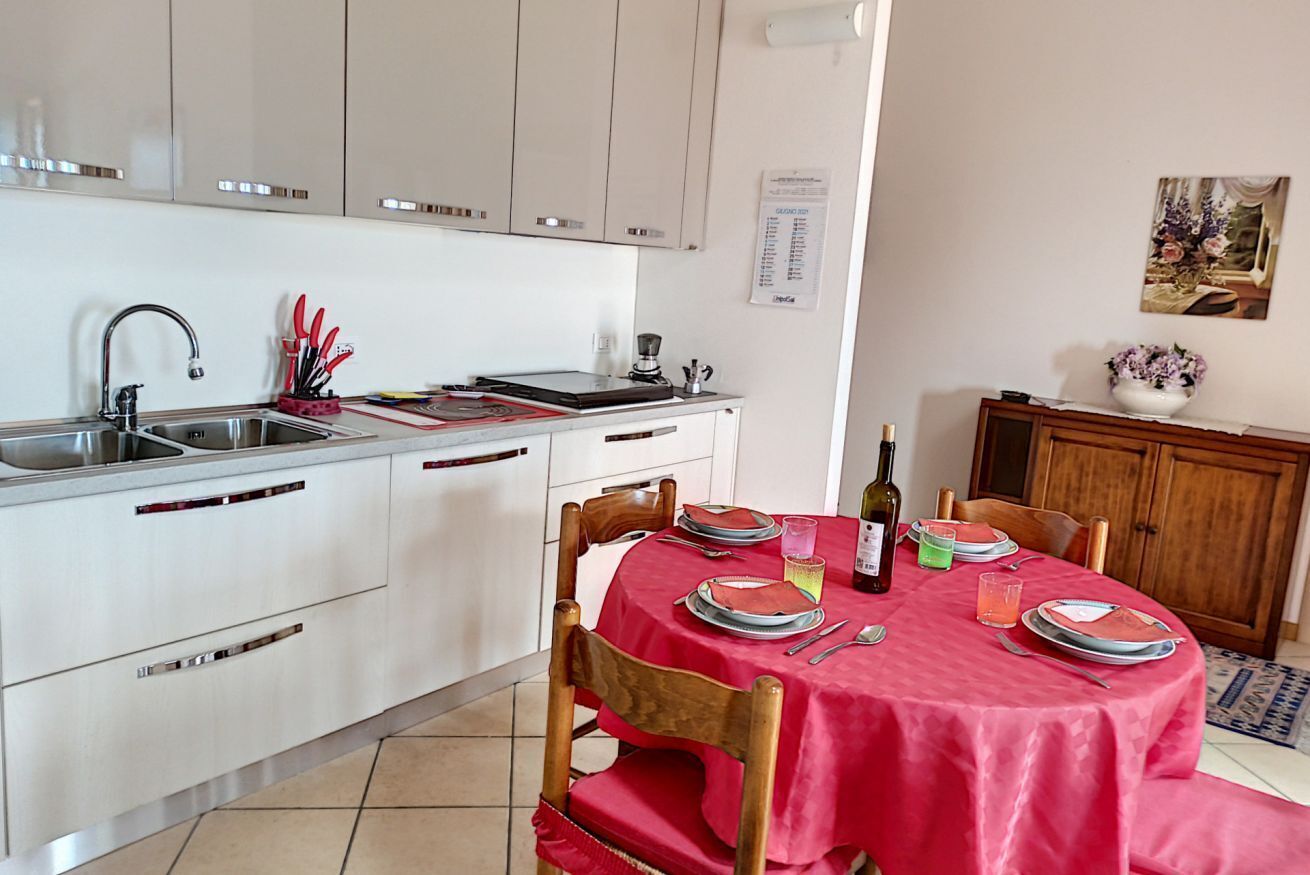 Una cocina con armarios blancos, un lavamanos y una zona de comedor con mantel rojo.