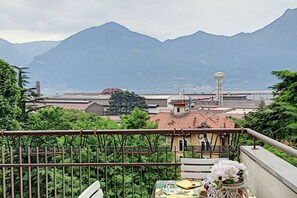 A balcony with a table set for dining, overlooking a mountainous landscape and a body of water.