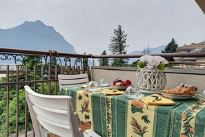 A balcony with a table set for two, featuring a floral tablecloth, a vase with flowers, and a plate of food.