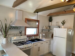 A kitchen with a gas stove, white cabinets, a refrigerator, and a window with blinds. - Contemporary Cottage in the heart of Mandeville (Mandeville)