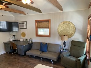 A modern living room with a sofa, a desk, a chair, a television, and a decorative wall piece. - Contemporary Cottage in the heart of Mandeville (Mandeville)
