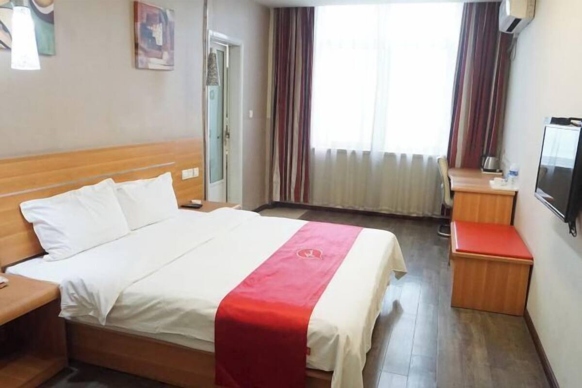 Ett hotellrum med en säng, ett skrivbord, en stol, en tv och ett fönster med gardiner.
