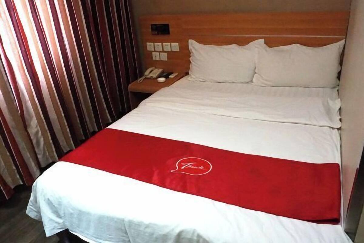 Ett hotellrum med en säng, ett nattduksbord med en telefon och ett rött och vitt sängöverkast.