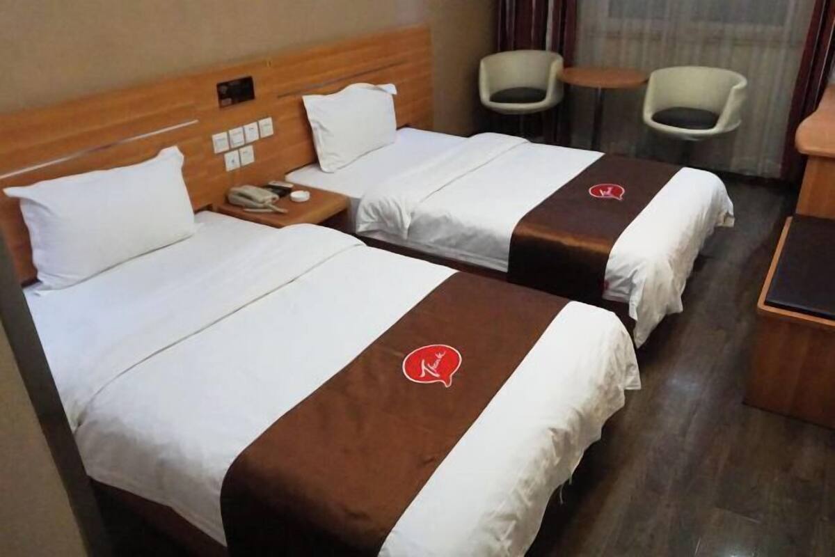 Ett hotellrum med två sängar, ett litet bord, två stolar och en sänggavel i trä.