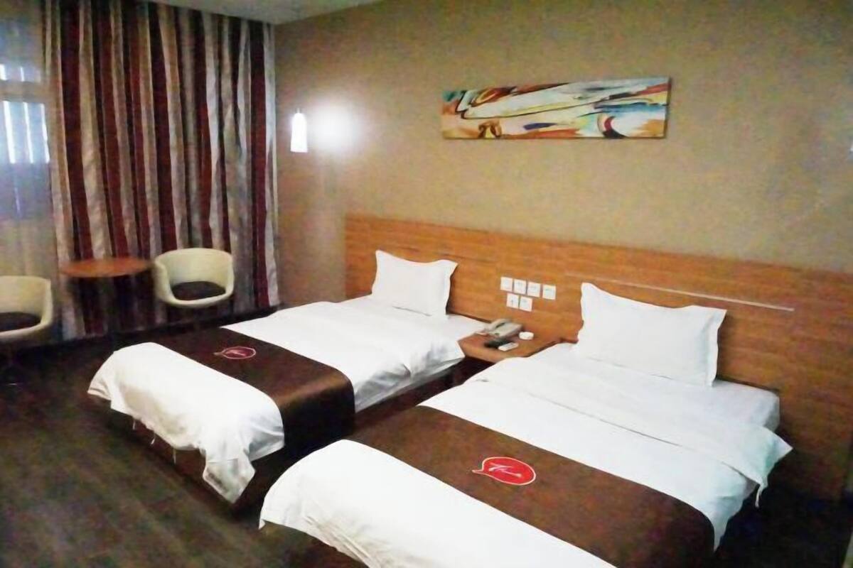 Ett hotellrum med två sängar, en sänggavel i trä, en tavla på väggen och två stolar.