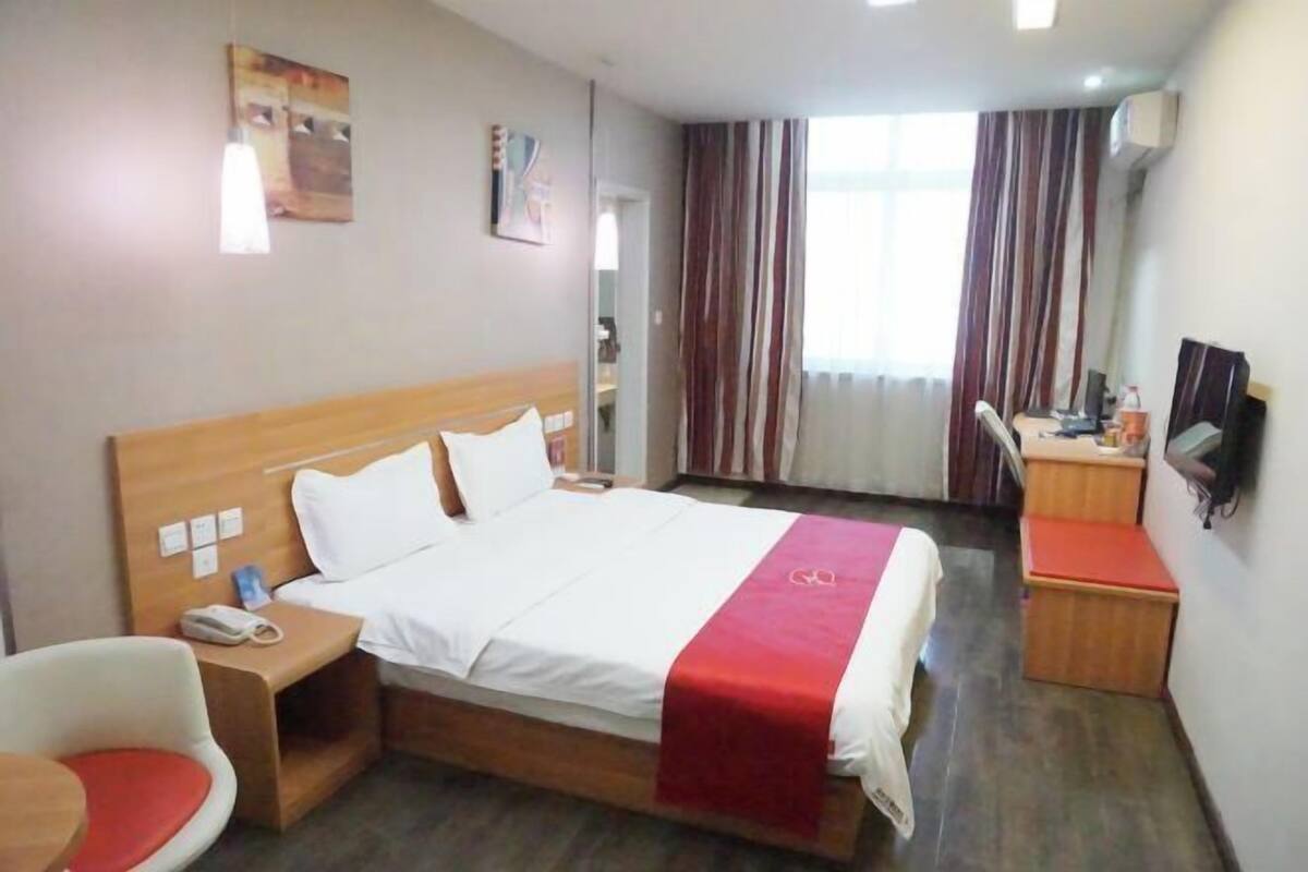 Ett hotellrum med en säng, ett nattduksbord, en stol, ett skrivbord, en tv och gardiner.
