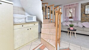 A kitchen with a microwave, a cream-colored cabinet, a staircase with wooden railings, and a living area with a sofa and a small table with a plant. - Holiday home Hana with air conditioning and sea views (Pula)