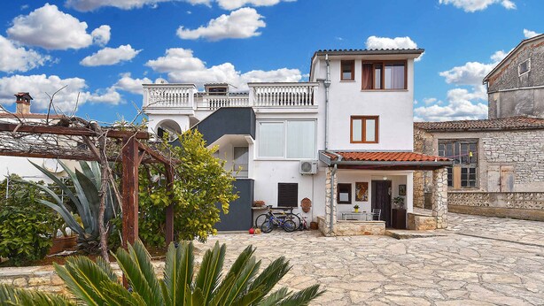 A two-story building with a balcony, a stone courtyard, and a potted plant in the foreground. - Holiday home Hana with air conditioning and sea views (Pula)