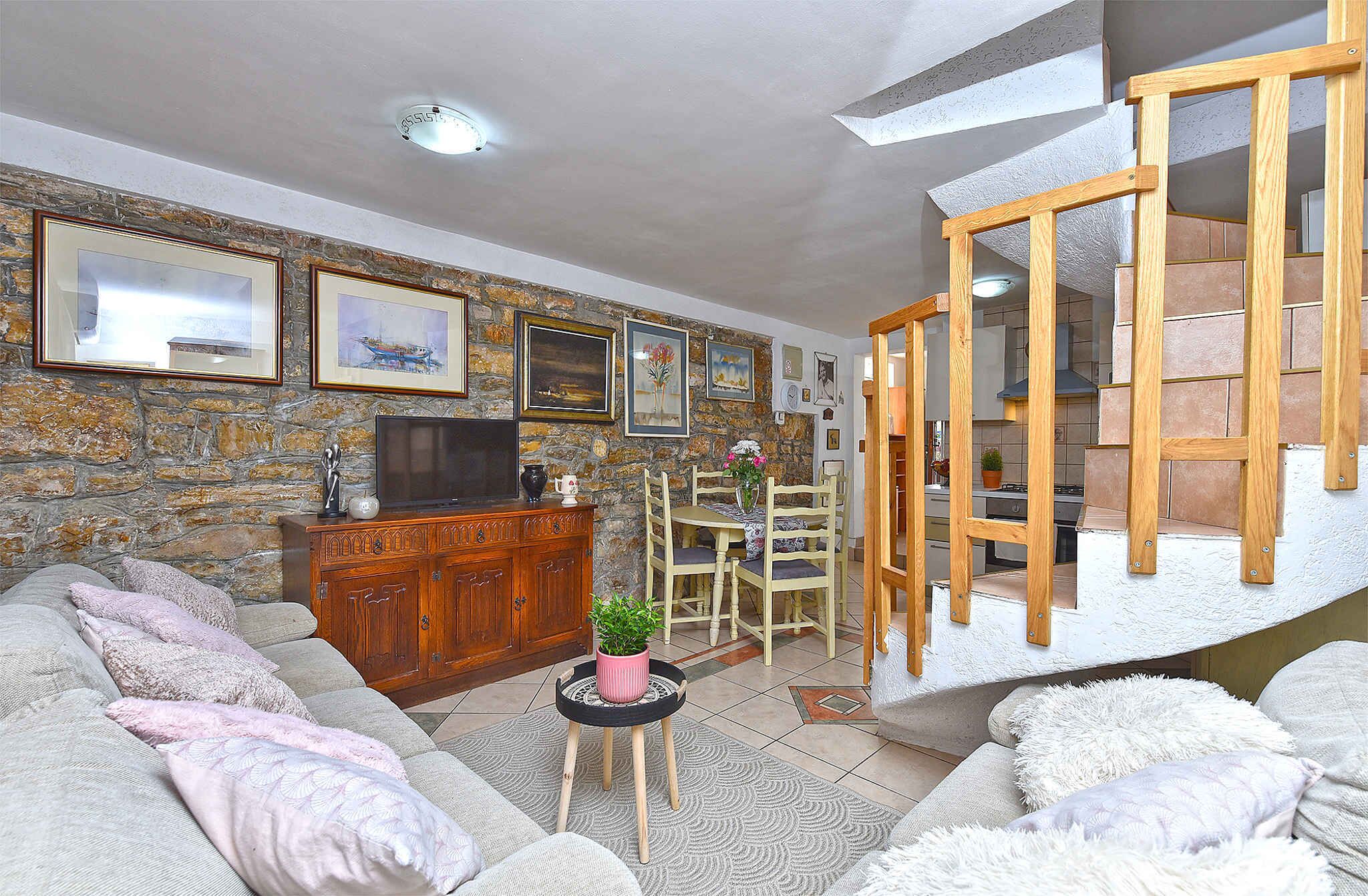 A living room with a stone wall, wooden furniture, a television, and a staircase.