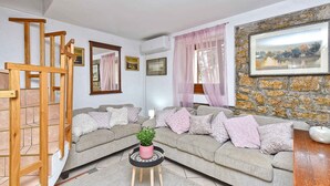 A living room with a wooden staircase, a grey sofa with cushions, a small table with a plant, and a stone wall with a framed picture. - Holiday home Hana with air conditioning and sea views (Pula)