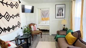 Una sala de estar con sofá, sillones, televisor, cama y ventana con cortinas.