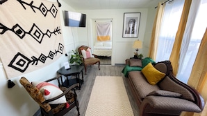 Una sala de estar con sofá, sillón y televisión en la pared.
