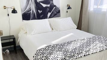 Ein Schlafzimmer mit einem Bett, einem Nachttisch, einer Lampe, einem Wandbild und einem Fenster mit Vorhängen.