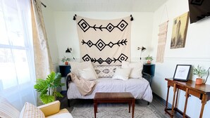 Un salón acogedor con un sofá amarillo, un tapete estampado y una cama con cabecero decorativo.