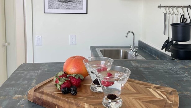 Una cocina con encimera de madera, un microondas y un lavabo. Hay una fotografía en blanco y negro enmarcada en la pared y un frutero con frutos rojos y una naranja sobre la encimera.