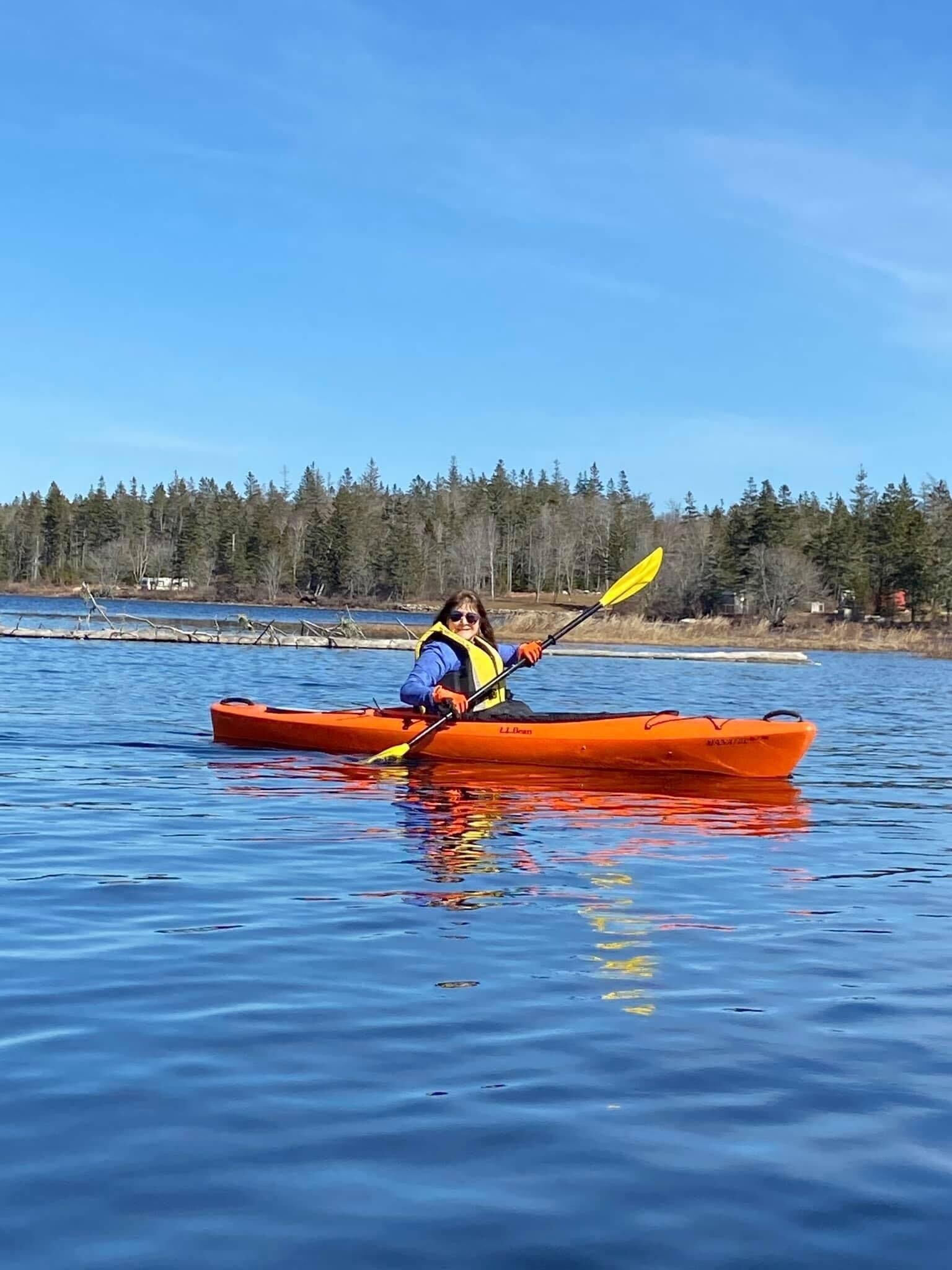 A person kayaking on a calm body of water with a forested shoreline in the background.