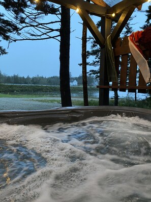 A hot tub with a wooden structure overhead, surrounded by trees and a view of a house in the background. - Lakefront country cabin with rustic charm overlooking lake (Salmon River)