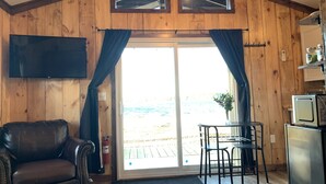 A cozy room with wooden walls, a leather chair, a small table with chairs, a television, and a sliding glass door leading to an outdoor area.