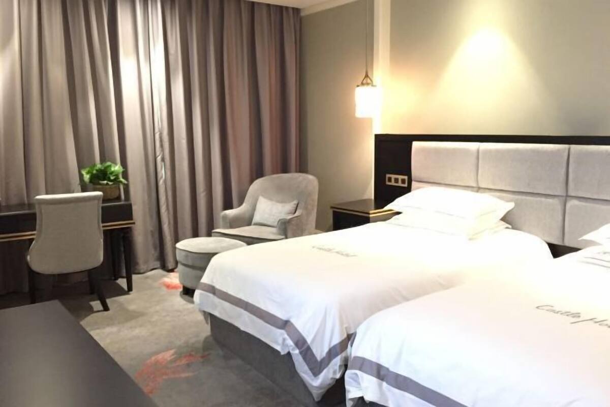 Ein Hotelzimmer mit einem großen Bett, einem Schreibtisch mit Stuhl, einem kleinen Tisch und einer Zimmerpflanze.