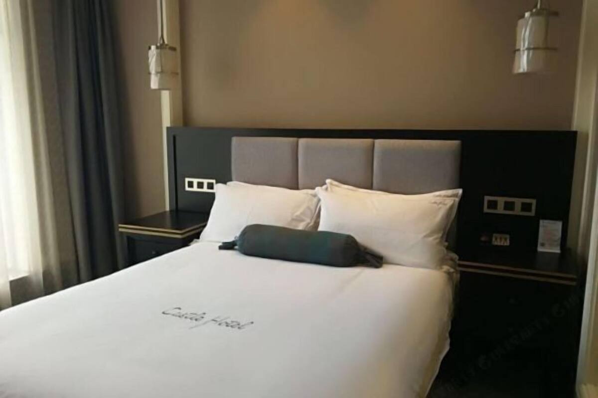 Ein Hotelzimmer mit einem großen Bett, einem Kopfteil mit Bedienfeld, einem Nachttisch und einer Lampe.