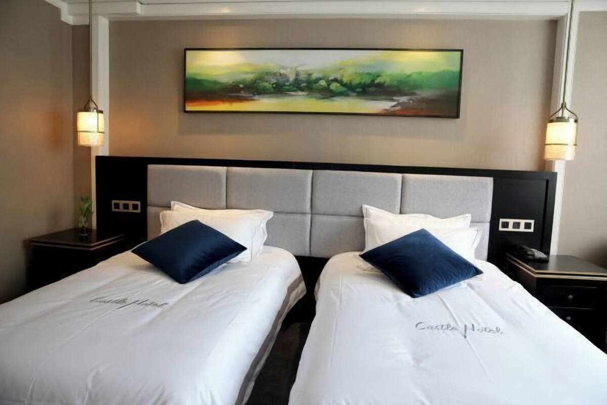 Ein Hotelzimmer mit zwei Betten, einem großen Gemälde an der Wand und Nachttischlampen.