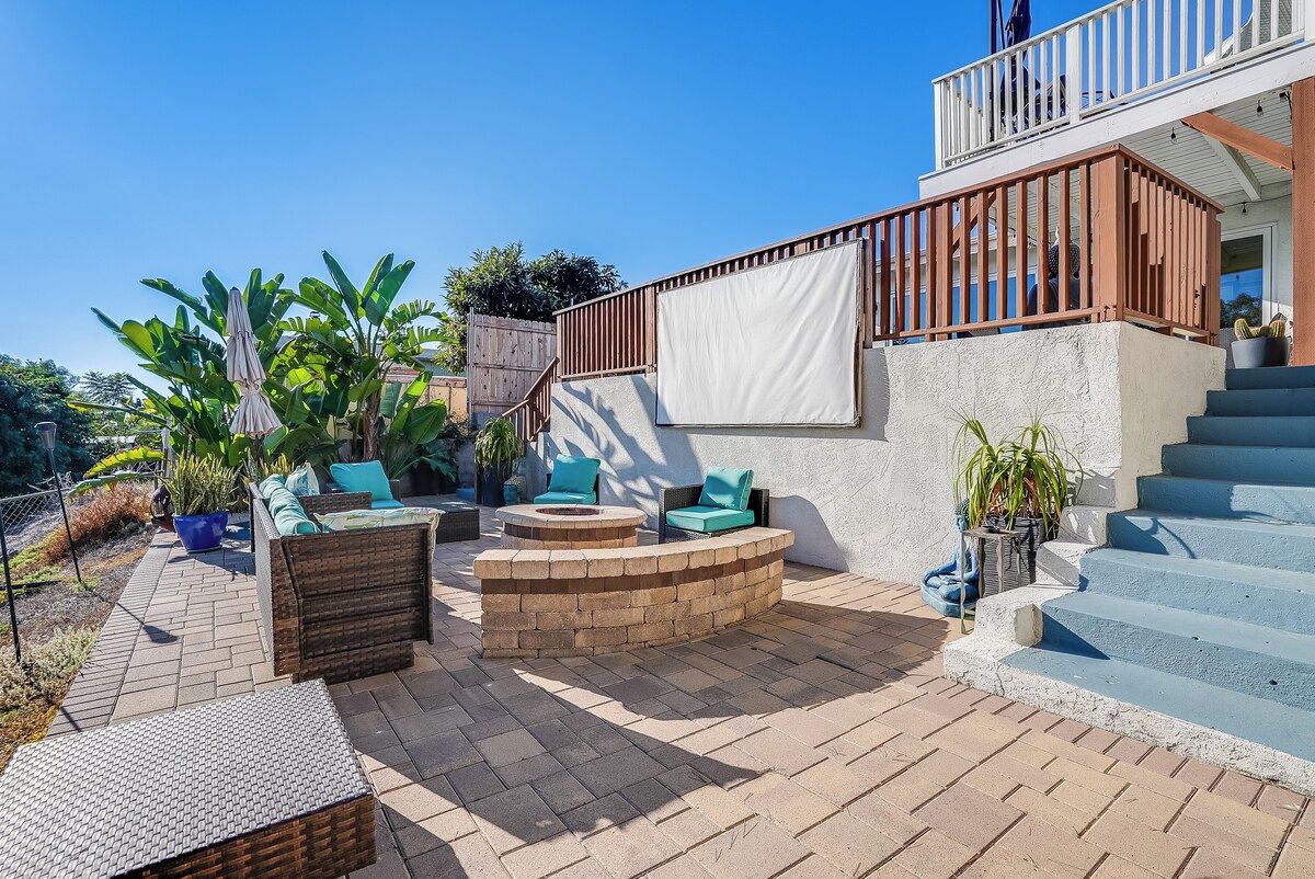 Eine Terrasse mit Gartenmöbeln, einem Feuerkorb und einer Treppe zu einem Balkon.