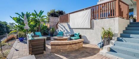Eine Terrasse mit Gartenmöbeln, einem Feuerkorb und einer Treppe zu einem Balkon.