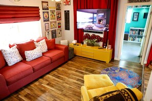 A living room with a red sofa, a yellow cabinet, and a television displaying a scenic view. - Canyon-View 4BR Home with Hot Tub & Fire Pit, 15 Min to Downtown (San Diego)