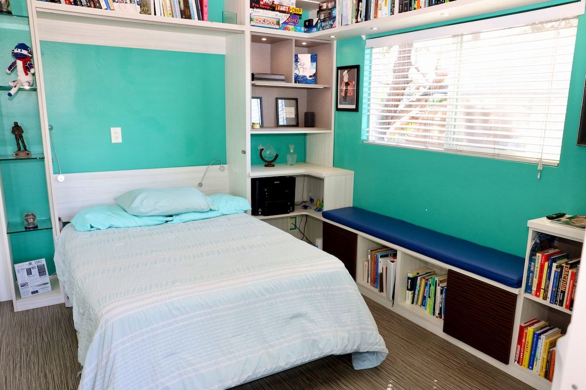A bedroom with a bed, a bookshelf, a desk, and a window.