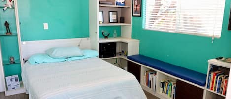 A bedroom with a bed, a bookshelf, a desk, and a window.
