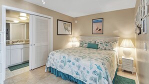 Un dormitorio con cama, mesita de noche, lámpara, cómoda, espejo y puerta.