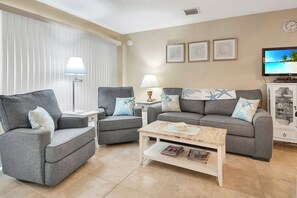 A living room with two grey sofas, a coffee table, a TV, and framed pictures on the wall.
