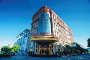Un hotel de varios pisos con una imponente torre de reloj, un amplio frente de cristal y una entrada majestuosa.