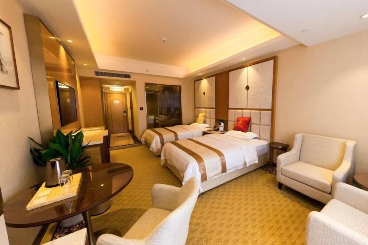 A hotel room with two beds, a desk with a chair, a sofa, and a large mirror.