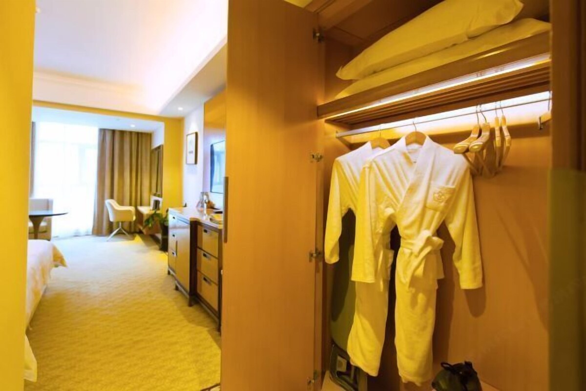 A hotel room with a bed, a desk, a chair, and a robe rack with robes.