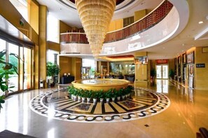 A spacious lobby with a central fountain, a chandelier, and a circular patterned floor. - March Flower International Hotel (Hechi)
